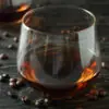 a snifter of bourbon-flavored coffee on a dark wood surface with coffee beans around it to represent bourbon infused coffee