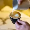 a hand holding a cup of espresso while the other pours milk into it showing the Difference Between Espresso Roast and Regular Roast